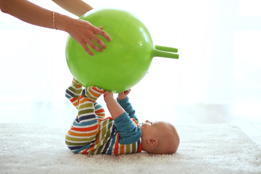 Baby playing with gymnastic ball with mother at home