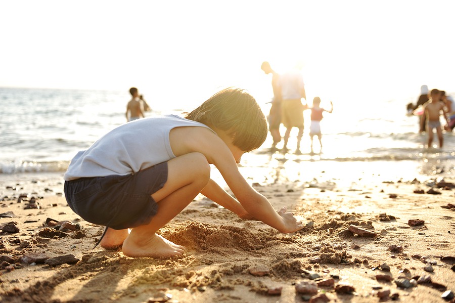 Kid on beach in sand playing, people around, summer hot nice tim
